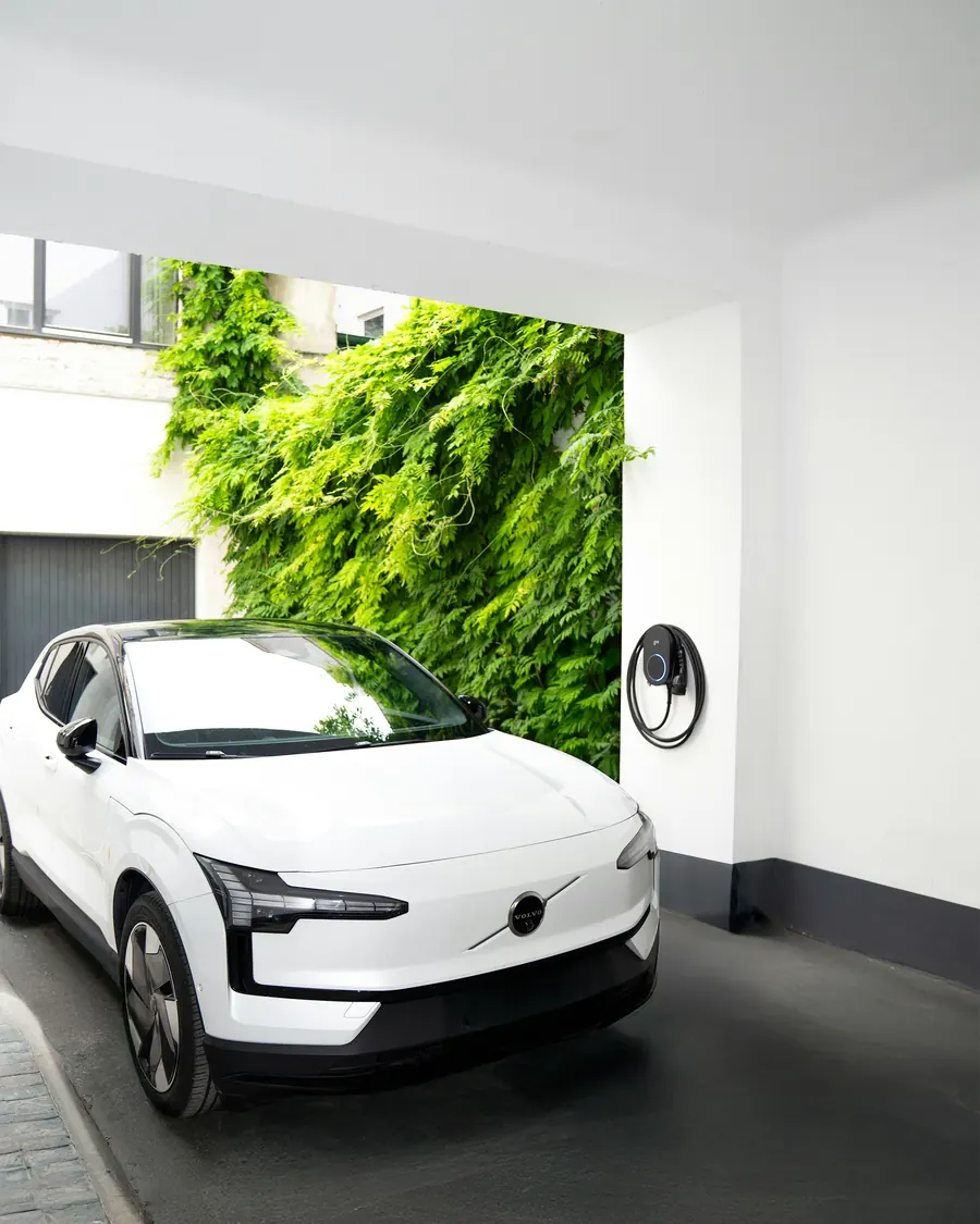 Weißes Elektroauto lädt an einer wandmontierten go-e-Wallbox in einer Hofeinfahrt